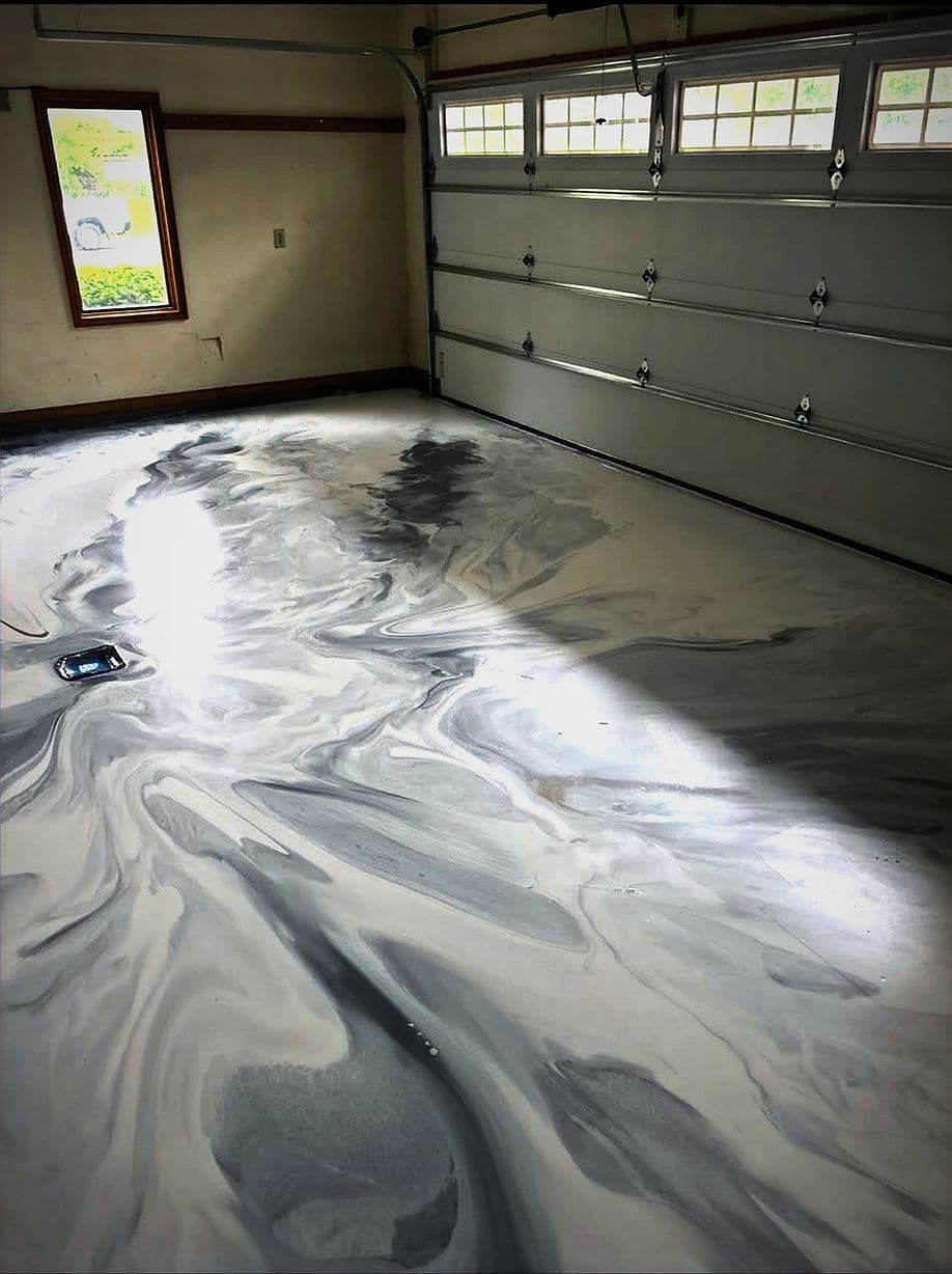 Modern garage floor with a sleek, marbled gray and white epoxy finish. Bright natural light illuminates.