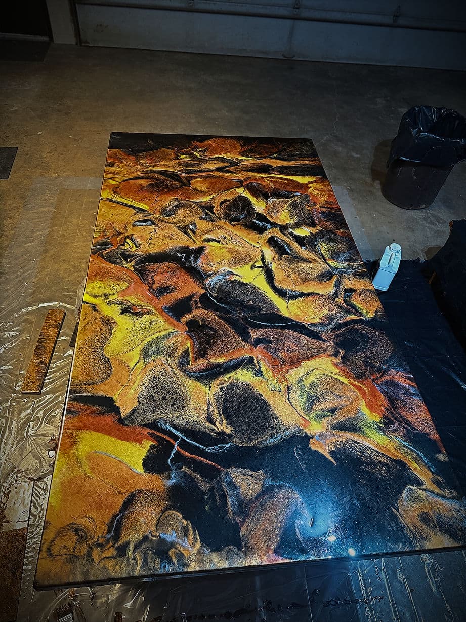 Abstract epoxy resin art featuring vibrant orange and black swirls on a textured surface.