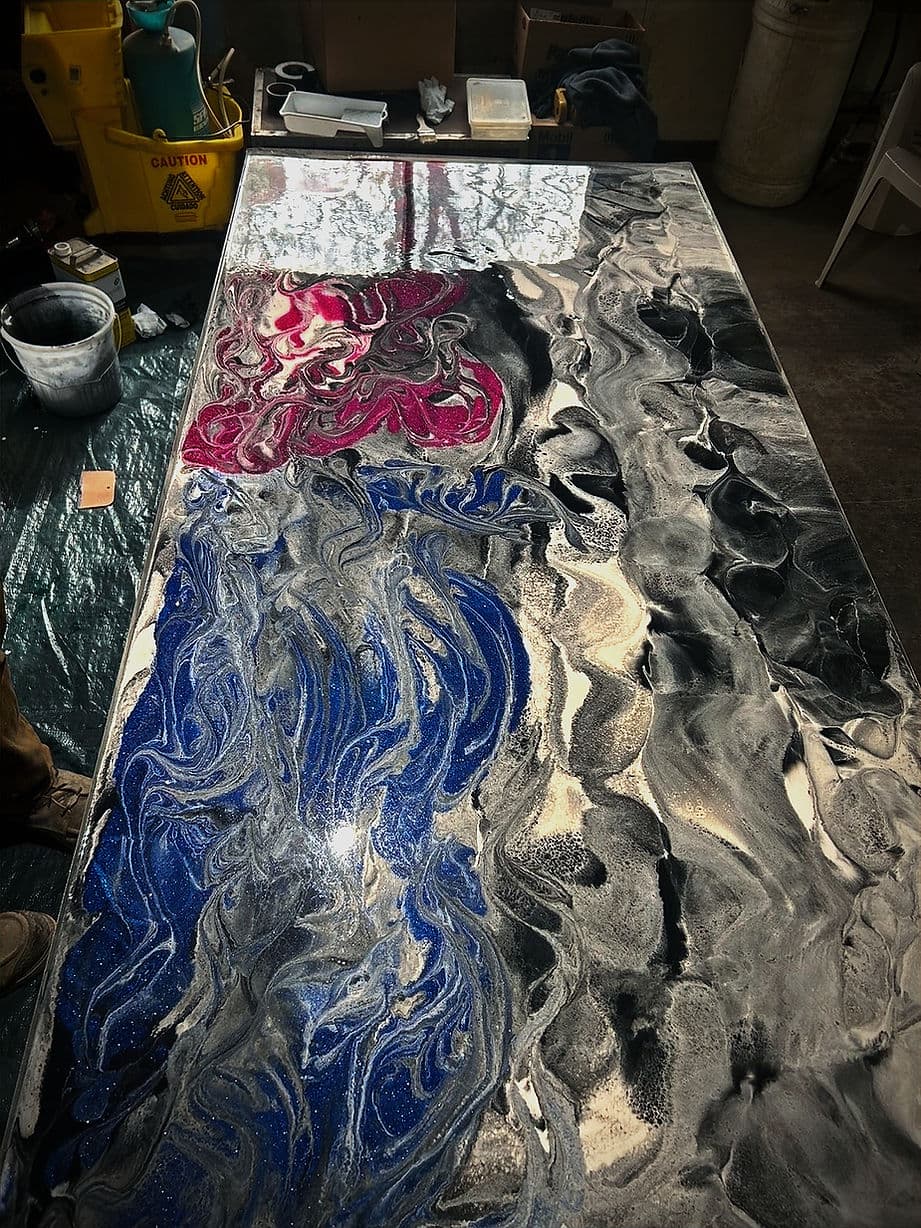 Colorful abstract epoxy resin art on a table featuring blue, black, and pink swirling patterns.